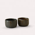 Two small dark brown ribbed ceramic cups with a glossy finish.