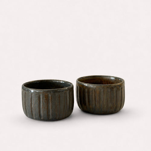 Two small dark brown ribbed ceramic cups with a glossy finish.