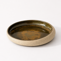 A round ceramic shallow dish with a speckled beige exterior and a glossy dark brown and olive-green glazed interior.