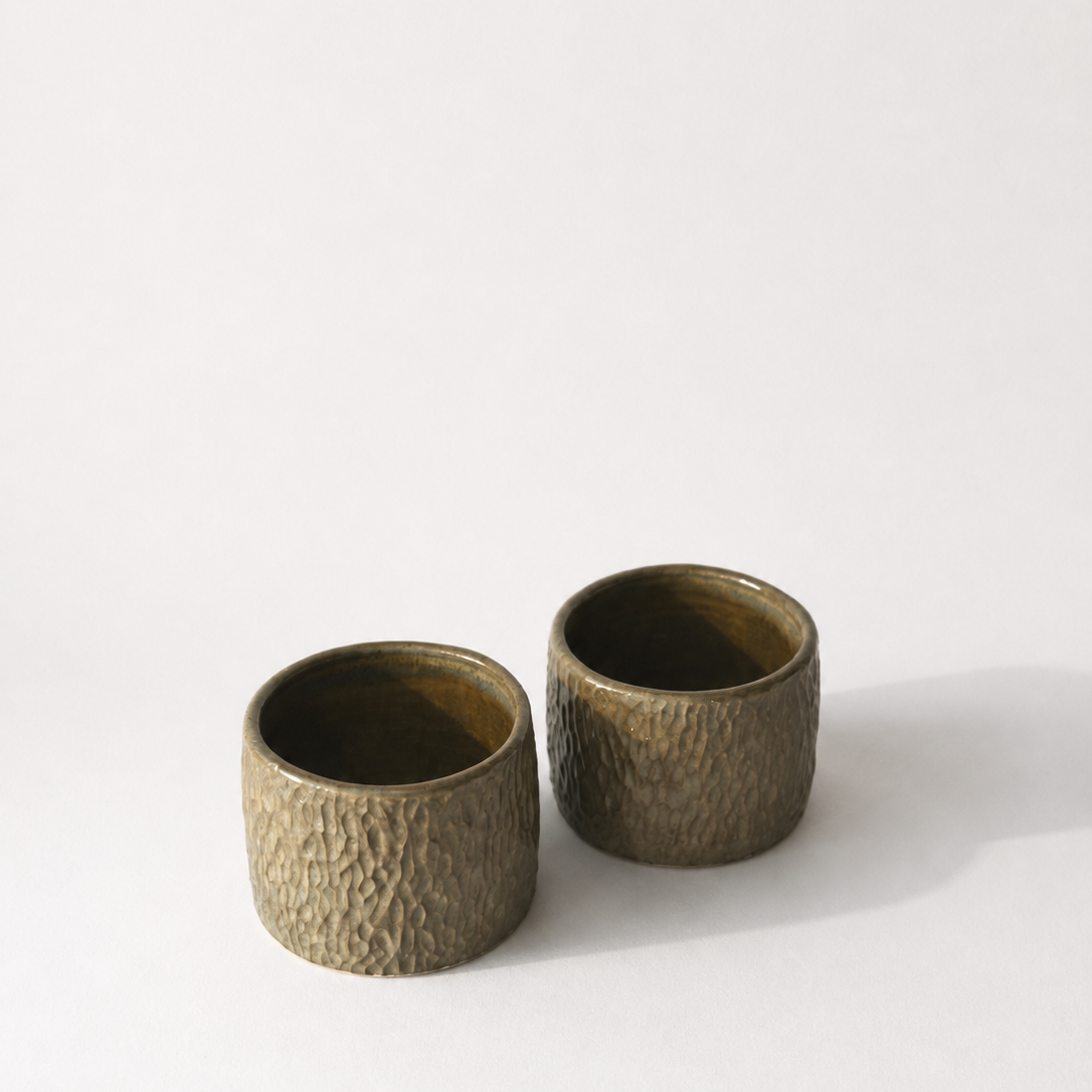 Two small textured ceramic cups with a metallic bronze/green finish.